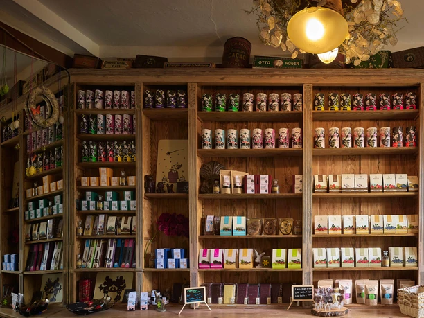 Dřevěné police v obchodě plné barevných balíčků čokolády a čaje; příjemná atmosféra s měkkým osvětlením.