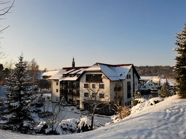 Hotel & Gasthof "Zur Post" Velká budova s červenými střechami je obklopena zasněženými stromy pod modrou oblohou při západu slunce.