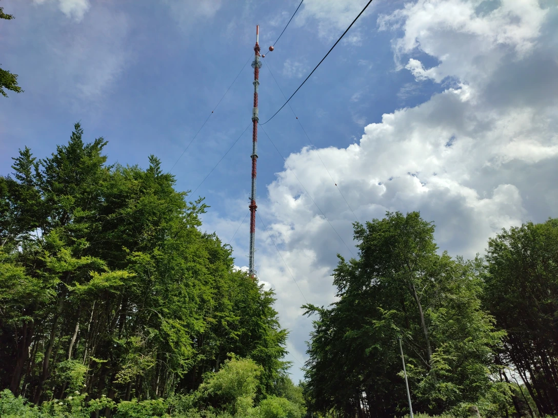 Teutoburger Wald / Detmold / Bielstein Ein hoher Sendemast ragt über grüne Baumwipfel, umgeben von blauem Himmel und weißen Wolken.