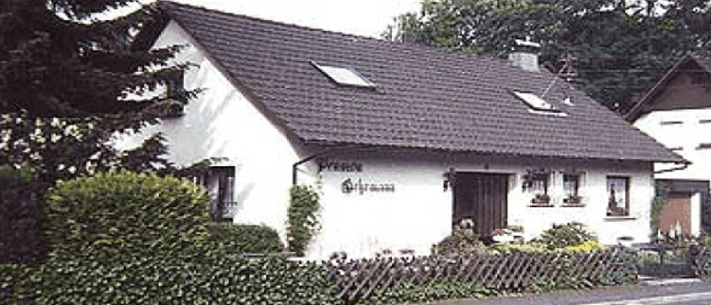 Pension_Gehrmann.jpg.png Ein weißes, einstöckiges Landhaus mit Satteldach, umgeben von grünem Buschwerk und Holzzaun.