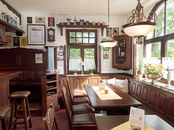 Gemütlicher Gastraum mit Holzmöbeln, dekorierten Wänden, großen Fenstern und einladendem Ambiente.