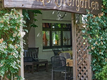 Gaststätte Hesse_Biergarten Eingang zu Conny's Biergarten mit begrüntem Torbogen, darunter Sitzgelegenheiten im Freien.