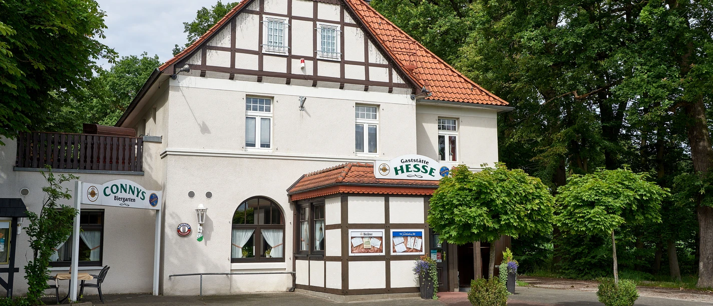 Gaststätte Hesse_Außenansicht Fachwerkhaus mit Restaurant Hesse, Eingangsbereich mit begrünten Blumenkübeln, umgeben von Bäumen.