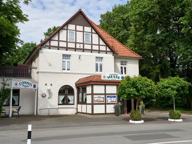 Gaststätte Hesse_Außenansicht Fachwerkhaus mit Restaurant Hesse, Eingangsbereich mit begrünten Blumenkübeln, umgeben von Bäumen.