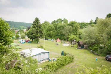 Campingplatz Eggewald in Horn-Bad Meinberg Grüner Campingplatz mit Zelten und Wohnwagen, umgeben von Bäumen, mit Spielplatz im Hintergrund.