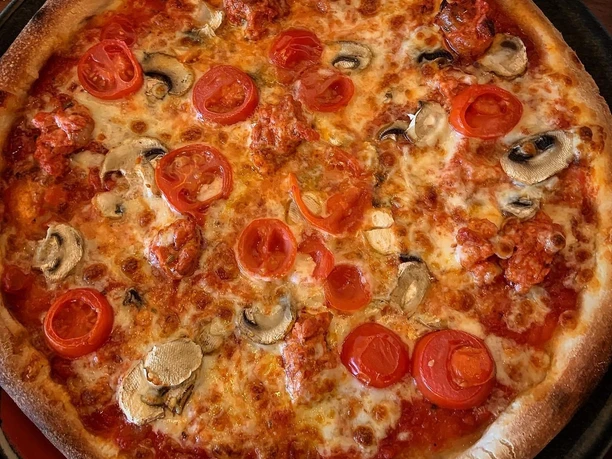 Pizza mit saftigen Tomatenscheiben, frischen Champignons und würziger Tomatensauce auf dünnem Teig.