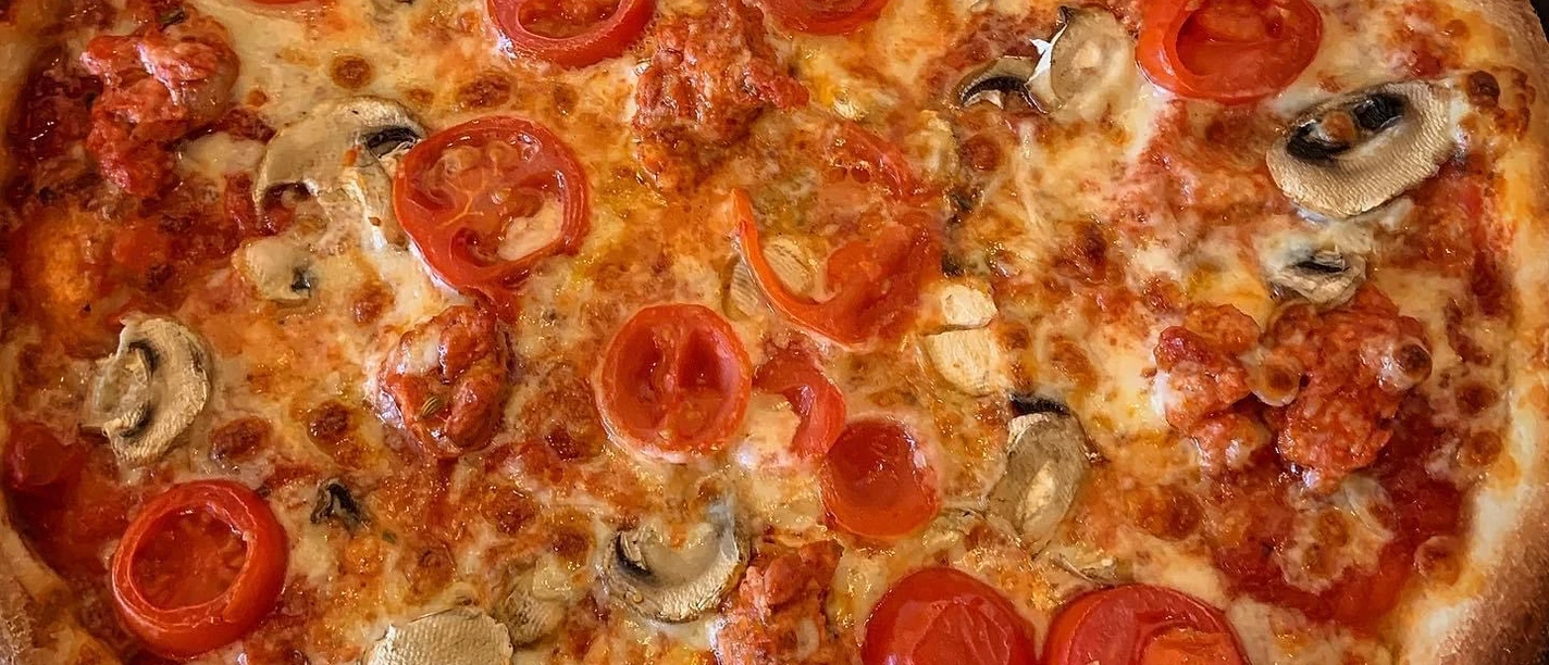 Pizza mit saftigen Tomatenscheiben, frischen Champignons und würziger Tomatensauce auf dünnem Teig.