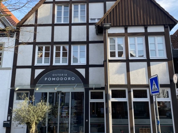 Fachwerkhaus mit "Osteria Pomodoro" im Erdgeschoss, blauer Himmel, geschlossene Fensterläden.