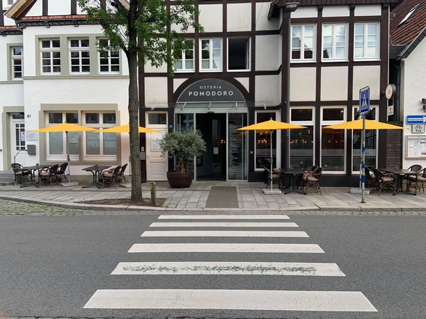 Die Fassade eines Fachwerkhauses mit der Osteria Pomodoro und gelben Sonnenschirmen davor.