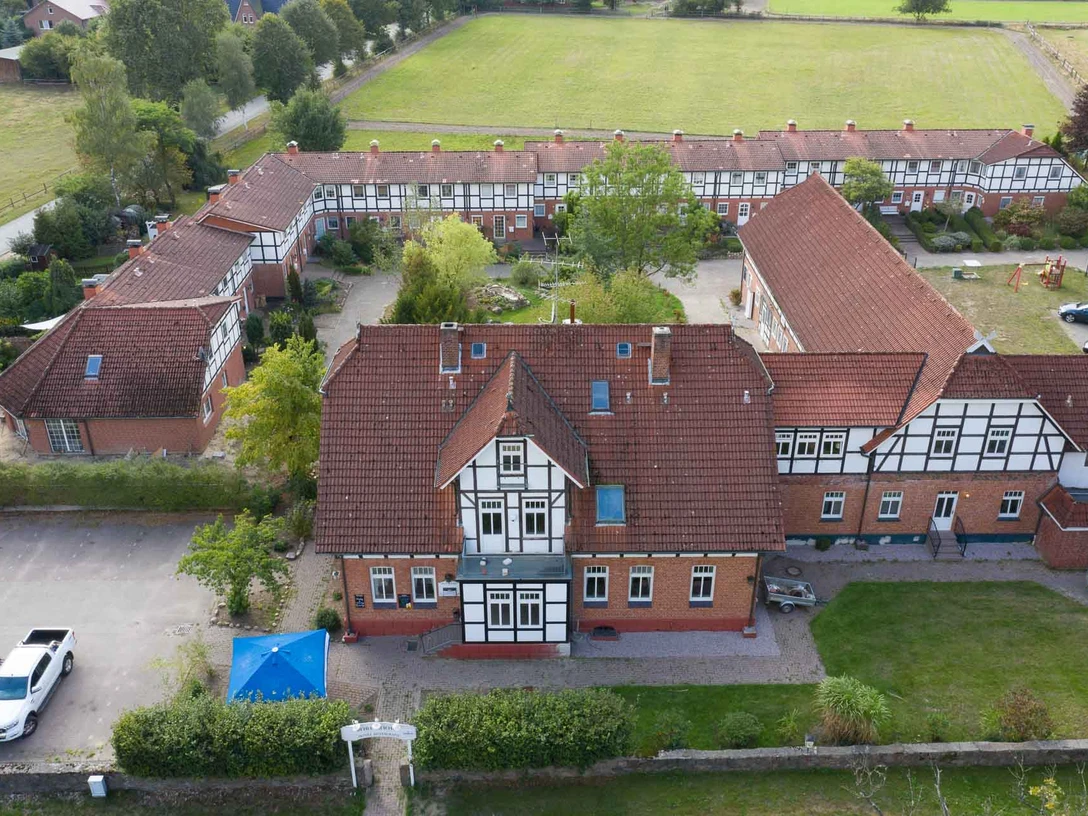 Außenansicht Das Bild zeigt eine historische Hofanlage in U-Form mit Fachwerkhäusern, umgeben von Grünflächen.