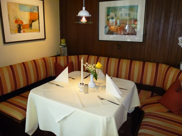 Hotel Zur Post_Gastraum Gemütliche Sitzecke in einem Restaurant mit rundem Tisch, gestreifte Polster, Blumen und Kunstbilder.