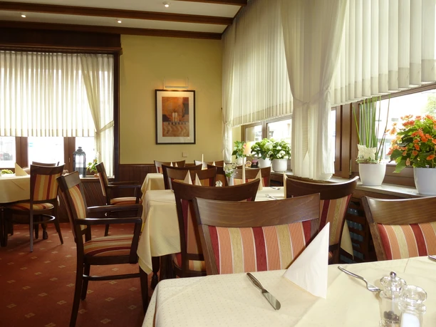 Ein gemütliches Restaurant mit Holzmöbeln, gedeckten Tischen und Pflanzen auf einer Fensterbank.