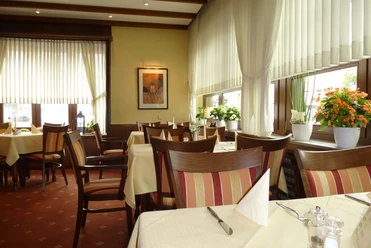 Hotel Zur Post_Gastraum Ein gemütliches Restaurant mit Holzmöbeln, gedeckten Tischen und Pflanzen auf einer Fensterbank.