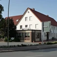 Zweistöckiges Gasthaus mit weißen Wänden, rotem Ziegeldach und umliegenden Bäumen an einer Straße.