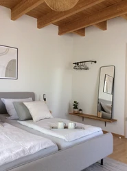 Modernes Schlafzimmer mit einem Doppelbett, helle Stoffe, Wandspiegel und Holzdecke sorgen für Gemütlichkeit.