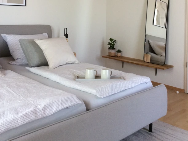 Modernes Schlafzimmer mit einem Doppelbett, helle Stoffe, Wandspiegel und Holzdecke sorgen für Gemütlichkeit.