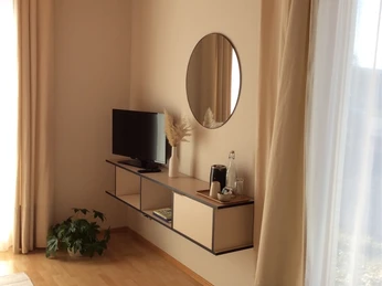 bed 'n' breakfast_Zimmer Modernes Wohnzimmer mit hellem Holzboden, kleinem TV auf einem schwebenden Regal und runden Spiegel.