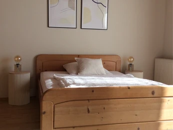 Helles Schlafzimmer mit einem holzfarbenen Doppelbett, zwei Nachttischen und moderner Wandkunst.