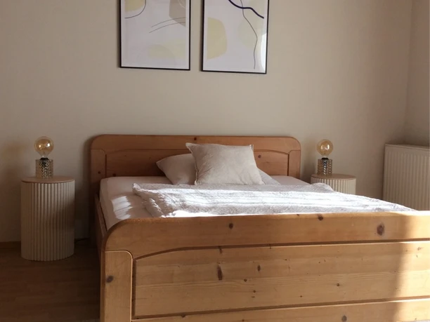 Helles Schlafzimmer mit einem holzfarbenen Doppelbett, zwei Nachttischen und moderner Wandkunst.