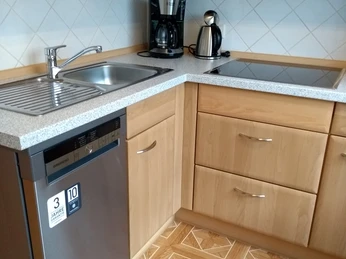 Holzküche mit Spülbecken, Geschirrspüler, Kaffeemaschine und Wasserkocher auf gemustertem Boden.