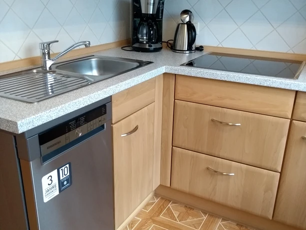 Küchenansicht Holzküche mit Spülbecken, Geschirrspüler, Kaffeemaschine und Wasserkocher auf gemustertem Boden.