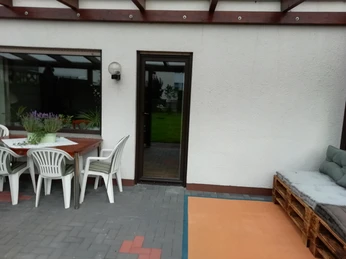 Überdachte Terrasse mit Tisch, Stühlen und einer Couch aus Paletten auf gepflastertem Boden.