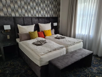 Schlafzimmer Zwei Einzelbetten mit farbigen Kissen und eleganter Tapete dahinter, Tageslicht dringt durch Vorhänge.