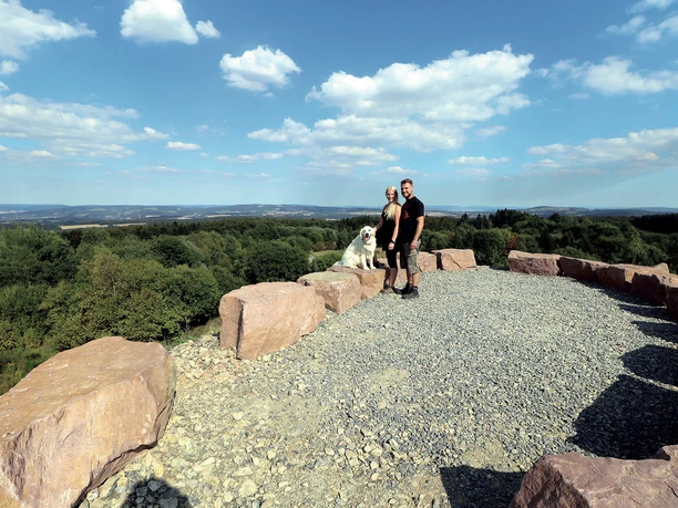 Paar mit Hund am Aussichtspunkt Steinberg mit weitem Blick über Wald und Hügelland
