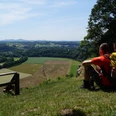 Ausblick vom Stachelberg Zwei Wanderer sitzen auf einer grünen Wiese mit Blick auf ein weites, hügeliges Tal unter blauem Himmel.