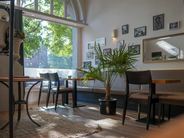 Modernes Café mit gemütlichem Interieur, Holzstühlen, Pflanzen und gerahmten Wandbildern.