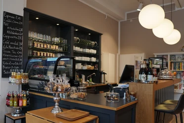 Café-Theke mit Glaskuppel, gefüllt mit Gebäck. Dahinter Regale mit Tassen und Gläsern.