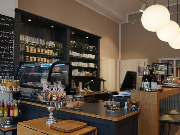 Café-Theke mit Glaskuppel, gefüllt mit Gebäck. Dahinter Regale mit Tassen und Gläsern.