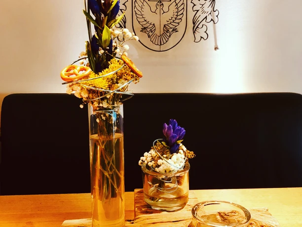 Blumenarrangement mit violetten Blüten in Vasen auf Holzpodest, daneben Teelicht, im modernen Ambiente.