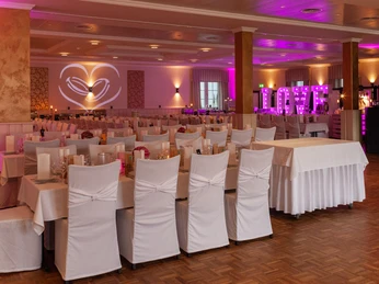Ein festlich dekorierter Hochzeitssaal mit weiß gedeckten Tischen und pinker Beleuchtung.