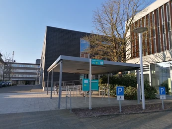 Eingangsbereich einer modernen Stadtbibliothek mit Fahrradständern und überdachtem Vorplatz.