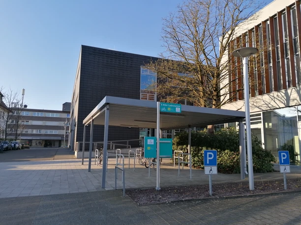 Eingangsbereich einer modernen Stadtbibliothek mit Fahrradständern und überdachtem Vorplatz.