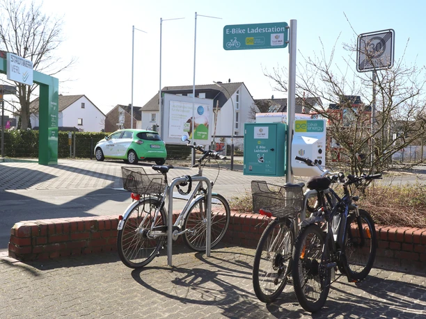 Ladestation auf dem Marktplatz Fahrräder parken bei einer E-Bike-Ladestation an einer Straße, im Hintergrund sind Häuser zu sehen.