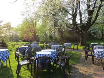 Garten mit Bäumen und mehreren Tischen und Stühlen, die mit blau-weißen Tischdecken bedeckt sind.