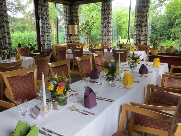 Ein elegant gedeckter Raum für eine Feier, umgeben von grüner Natur durch große Fenster.