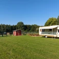 Wohnmobilstellplatz Straußenhof Möller Wohnmobil auf grünem Stellplatz, daneben eine rote Holzhütte; Bäume im Hintergrund bei klarem Himmel.