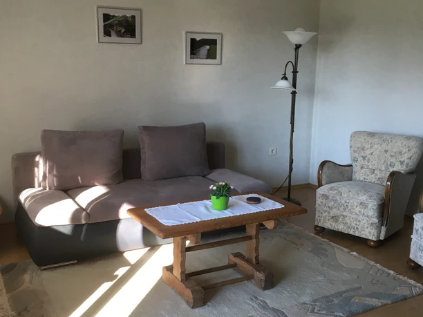 Ferienwohnung Ruhepol Helles Wohnzimmer mit grauem Sofa, Holz-Couchtisch, gemütlichem Sessel und zwei gerahmten Bildern.