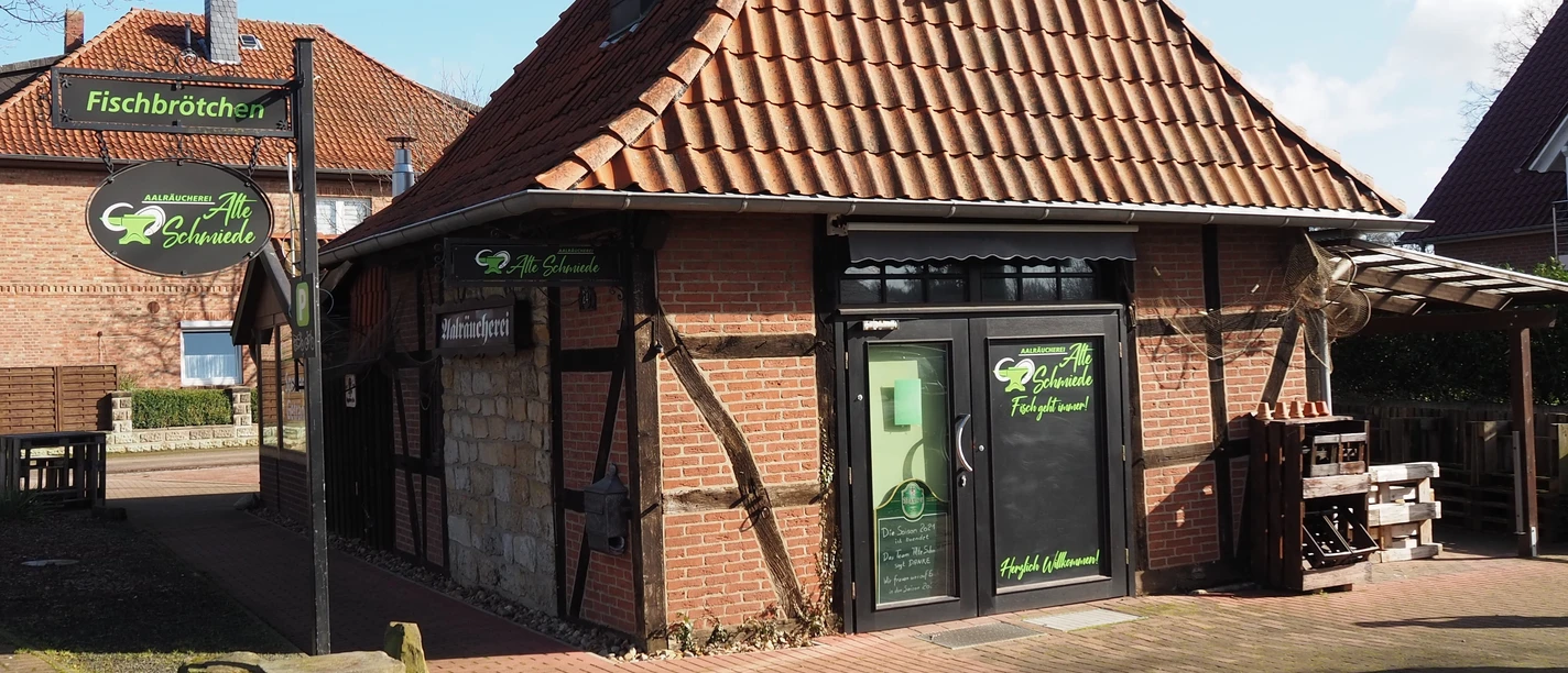 Alte Schmiede Ein traditionelles Fachwerkgebäude mit rotem Ziegeldach und grünen Schildern einer Schmiede.