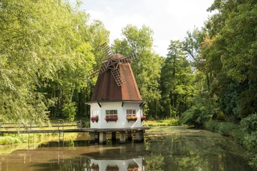 Heidberger Mühle im Ittertal bei Haan Historische Windmühle im Grünen, umgeben von Bäumen, mit einem kleinen Teich im Vordergrund.