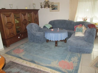 Wohnzimmer mit blauen Polstermöbeln, Holzschrank, Teppich mit Blumenmuster, hellem Boden und Dekor.