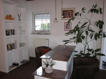 Ein Wohnzimmer mit moderner Dekoration, einem kleinen Bartisch, Regalen und einem großen Pflanzengewächs.