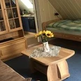 Schlaf_-_und_Wohnraum Dräger.jpeg Ein kombinierter Wohn- und Schlafbereich mit Holzmöbeln, Blumen auf dem Tisch und einem Einzelbett.