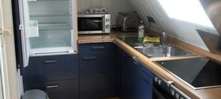 Moderne Küche in Dachgeschosswohnung mit offenem Kühlschrank, Spüle, Herd und Mikrowelle.