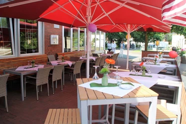 Zum Doppe_Biergarten Ein gemütlicher Außenbereich eines Cafés mit Tischen, Stühlen und roten Sonnenschirmen an sonnigem Tag.
