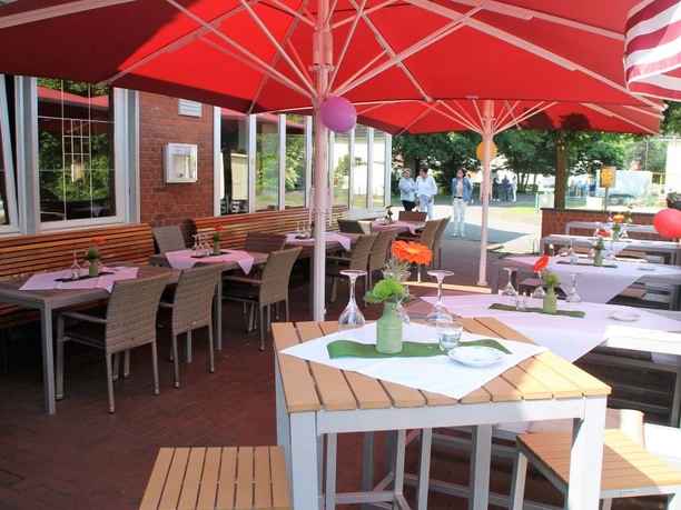 Zum Doppe_Biergarten Ein gemütlicher Außenbereich eines Cafés mit Tischen, Stühlen und roten Sonnenschirmen an sonnigem Tag.