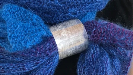 Taimi Design Breiter, gravierter Silberring mit feinem Muster umschließt einen blau-violetten Strickschal.